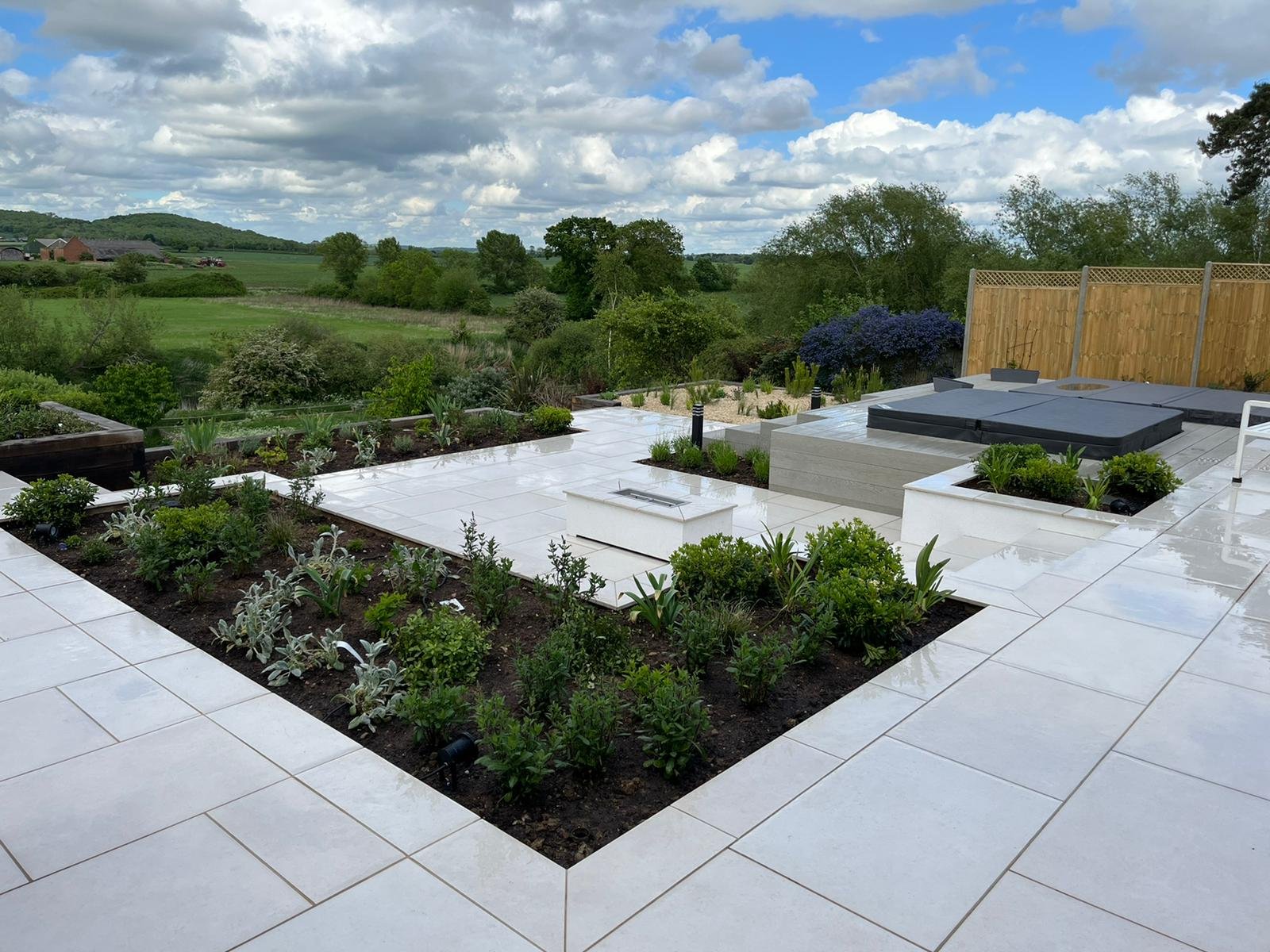 Rivermead in Bidford-on-Avon residential front and back garden re-design - Raised entertainment patio area, 2 hot tubs and a small sunken pool. White porcelain slabs with white grouting. Train sleeper stair case. Porcelain slab stair case. Custom height fencing. Sunken flower beds.