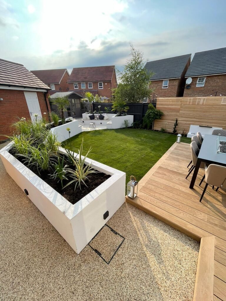 Taylor Landscape and Design Luxury Residential Landscaping Project in Warwickshire - White Raised Planting beds, with lighting and rendered finish. Raised custom decking, turf with slat fencing, resin pathway around the garden.