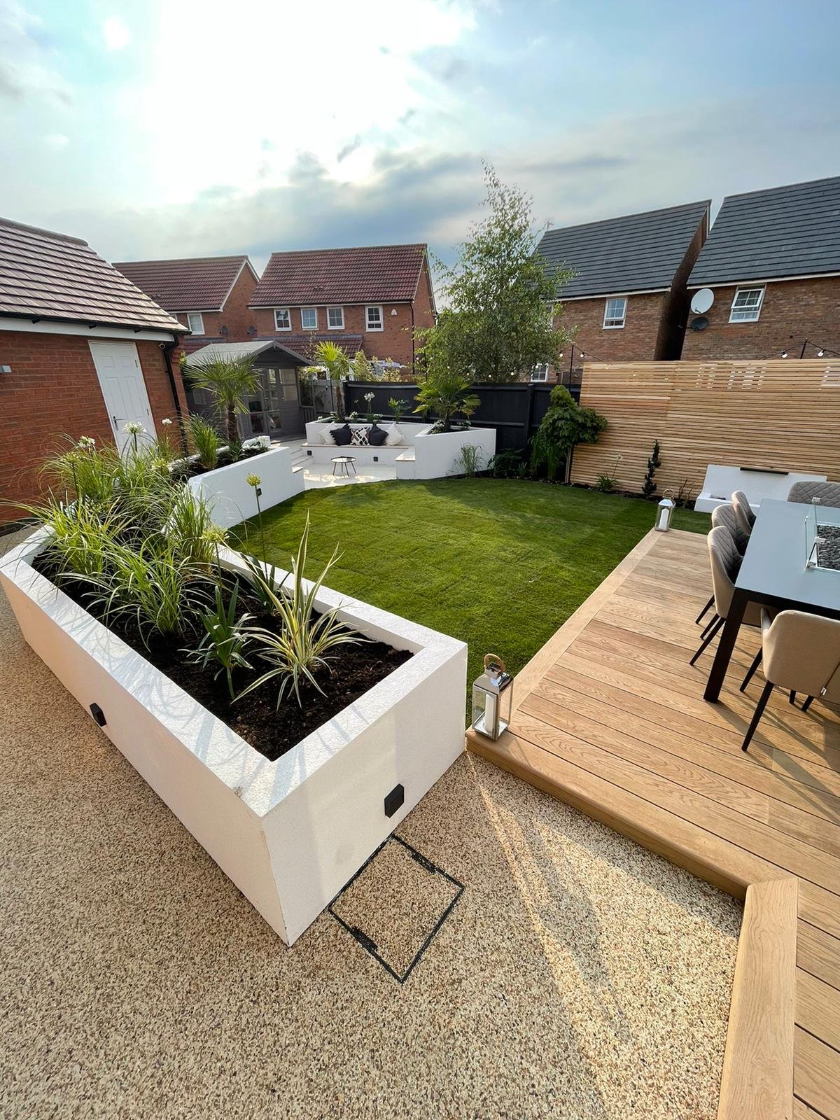Taylor Landscape and Design Luxury Residential Landscaping Project in Warwickshire - White Raised Planting beds, with lighting and rendered finish. Raised custom decking, turf with slat fencing, resin pathway around the garden.