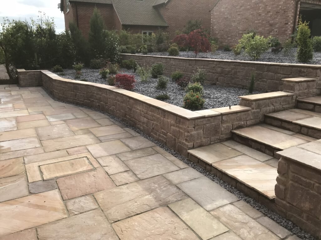 Multi-tiered patio design featuring Indian sandstone paving slabs, stone retaining walls, and terraced garden beds