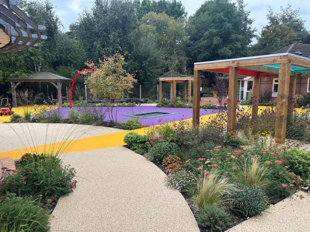 Acorn Hospice in Walsall Commercial Landscaping Project - Resin footpaths, wooden garden structure, outdoor pergola, climbing frames, new turf. New planting plan and flower beds. Stone pathway and patios. Flower beds with flowers and grasses.
