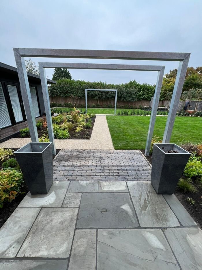 Modern garden landscape design in Warwickshire featuring bespoke steel archways, patio paving, and manicured turf